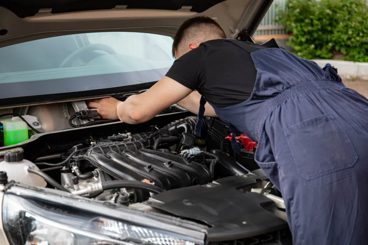 A mechanic performing maintenance work on a car's engine in an outdoor setting