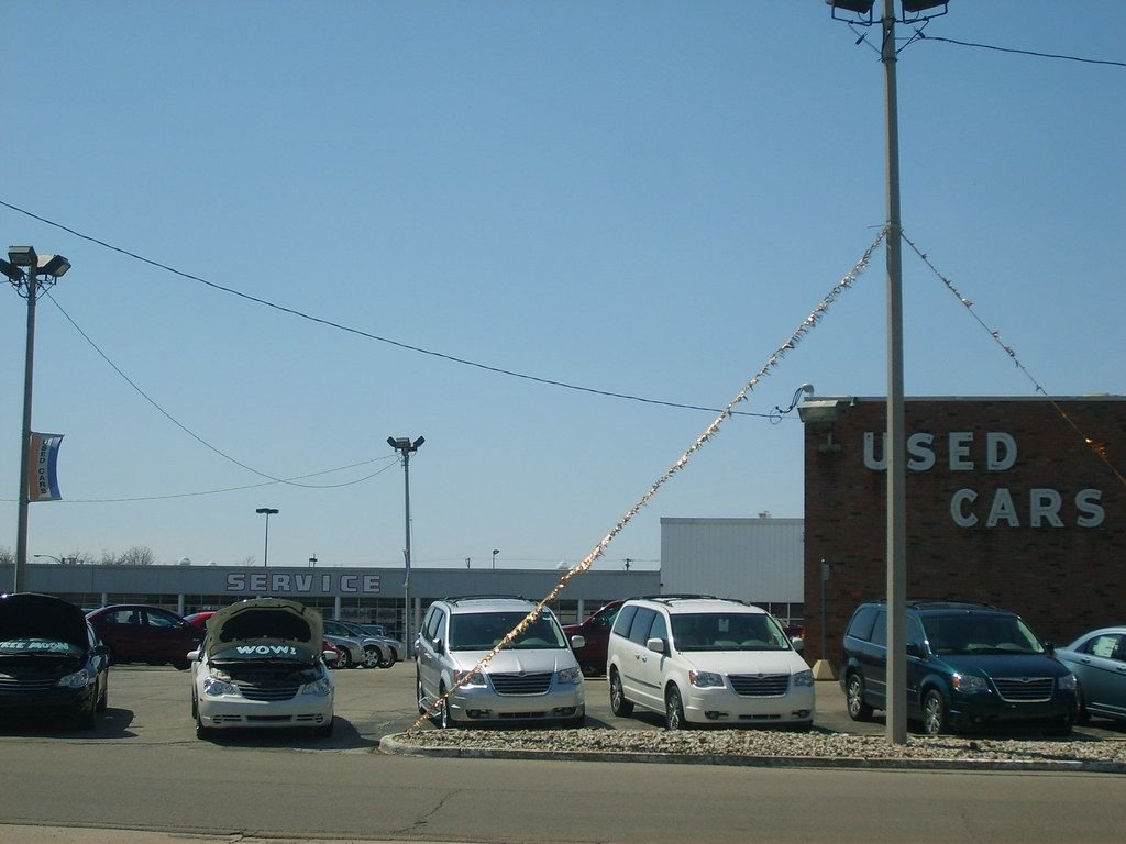 Dealer used car lot with minivans and sedans lined up under a USED CARS sign