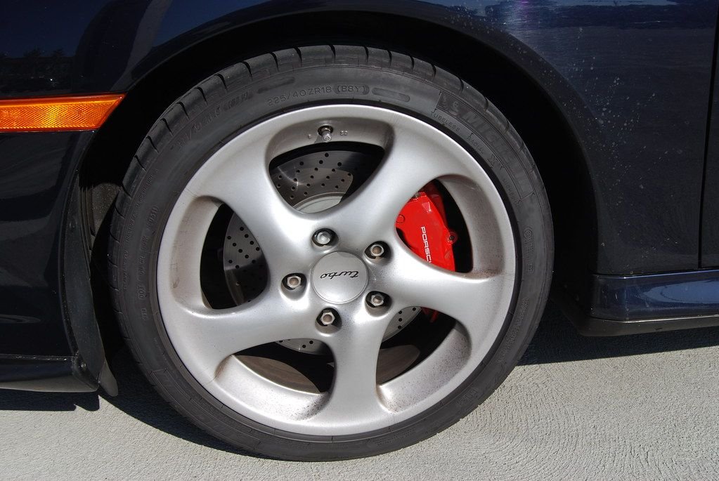 Red brake caliper visible behind an alloy wheel and drilled rotor on a sports car