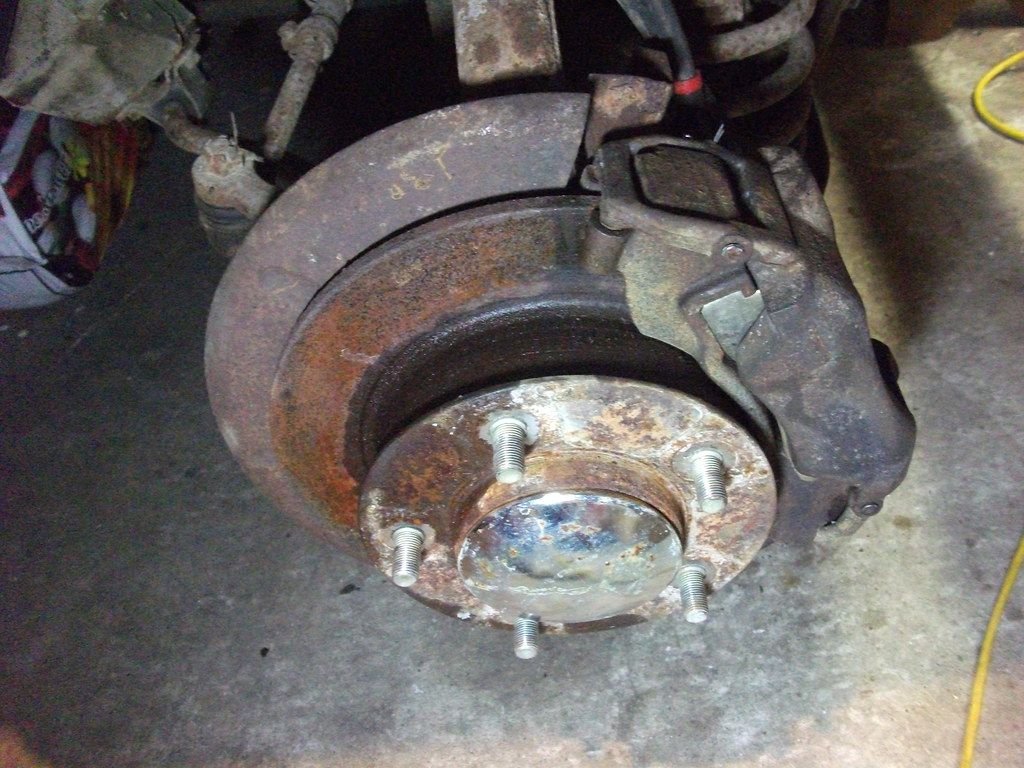 Rusty brake caliper and rotor on a car with the wheel removed, a common sight when a brake caliper is failing