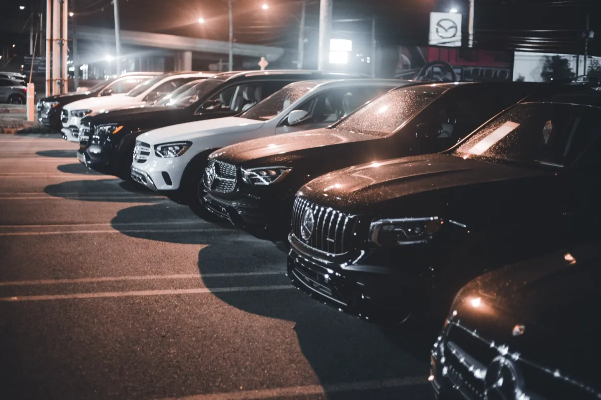 Row of luxury cars in a parking lot at night, illuminated by streetlights
