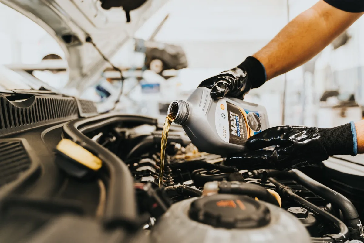 Close-up of a mechanic pouring engine oil into a car engine in an auto repair shop