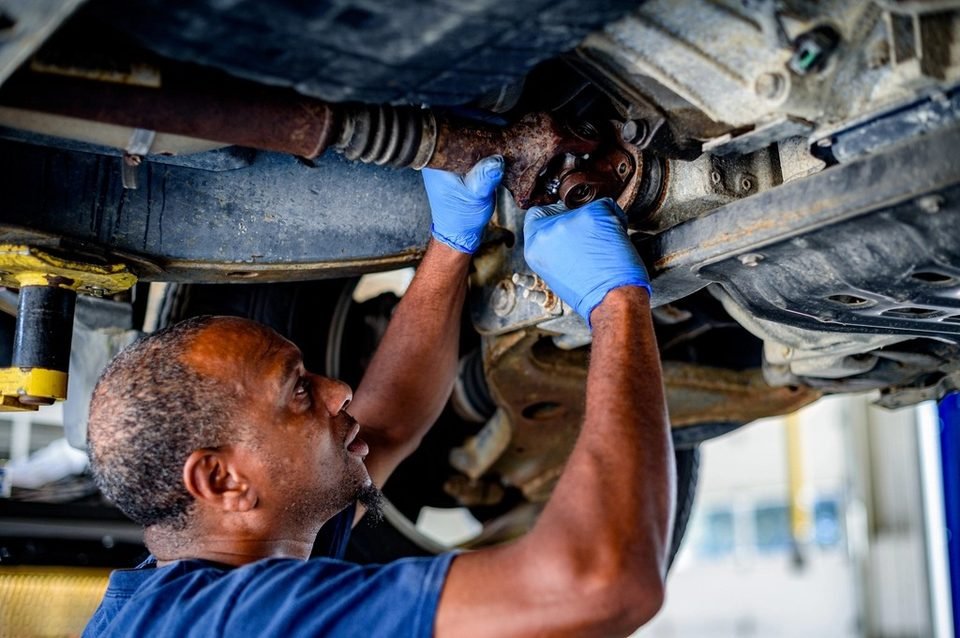 Mechanic working under a raised car on the front axle and CV joint area