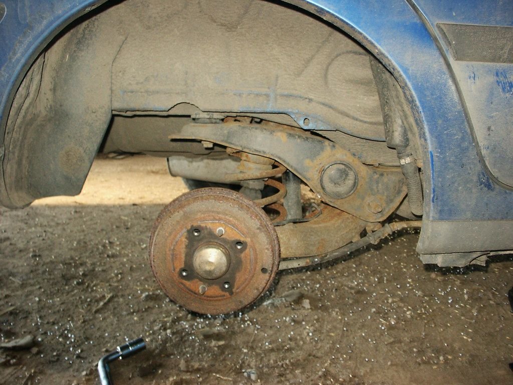 Worn rear brake drum on a car with the wheel removed, ready for drum brake replacement