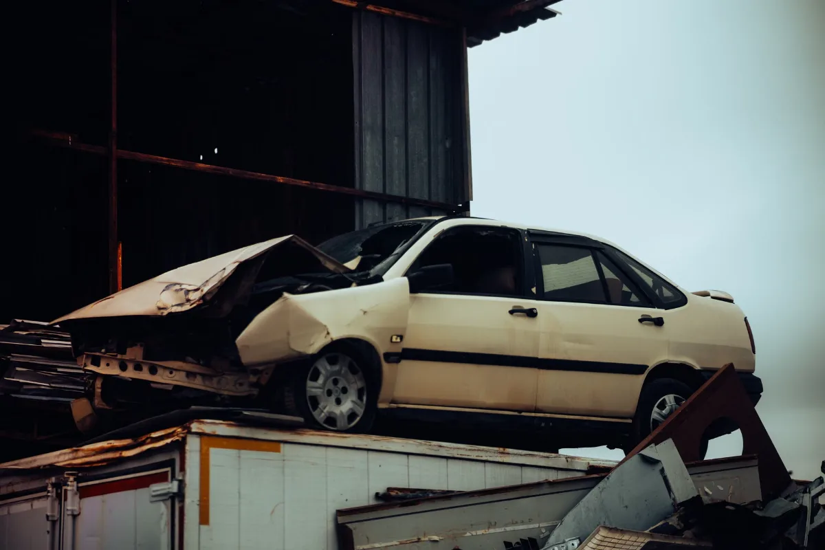 A damaged car sits atop a metal scrap heap, showing a scene of automotive decay