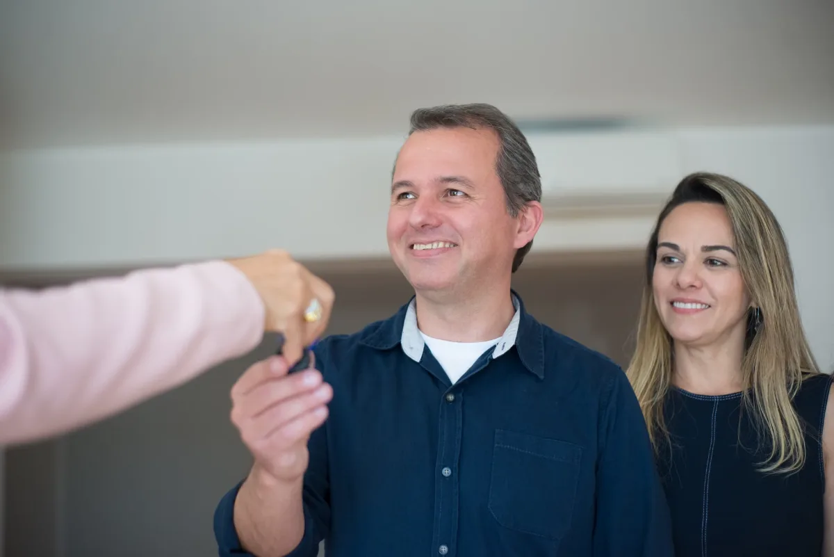 Smiling couple receiving keys, celebrating new home purchase indoors