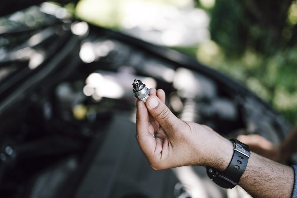 Mechanic holding a small engine part over an open engine bay during routine maintenance