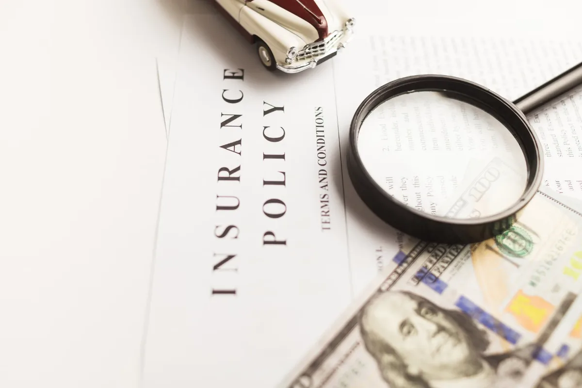 Close-up image of an insurance policy with a magnifying glass, money, and toy car